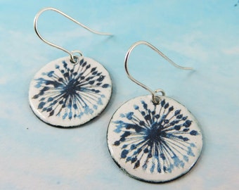 May include: A pair of silver dangle earrings with white enamel round discs featuring a blue and black abstract floral design.