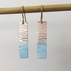 May include: A pair of dangle earrings with a light blue and copper design. The earrings are made of metal and have a rectangular shape.
