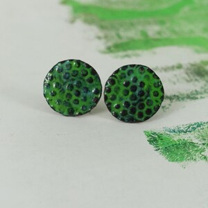 May include: A pair of round stud earrings. The earrings are a vibrant green with a textured surface and small, dark green dots. The earrings are set against a white background with green accents.