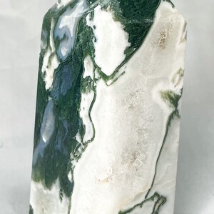 May include: A green and white agate crystal point with a natural, rough texture. The crystal is a light green colour with white swirls and patterns.