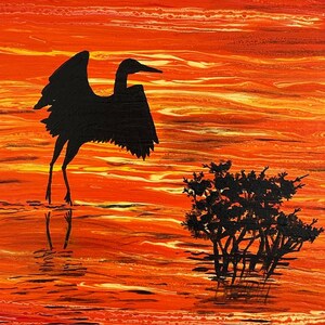 Puede incluir: Una silueta negra de un pájaro con las alas extendidas se encuentra en un cuerpo de agua con una silueta negra de un arbusto en el fondo. El agua está pintada en tonos de naranja, rojo y amarillo.