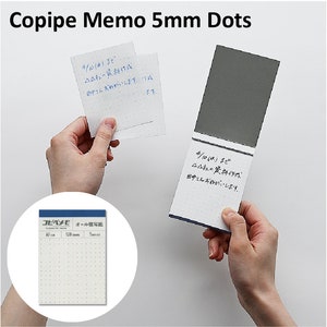 Puede incluir: Un bloc de notas azul y blanco con puntos de 5 mm. El bloc de notas está abierto y tiene una cubierta gris. El bloc de notas está etiquetado como "Copipe Memo 5mm Dots".