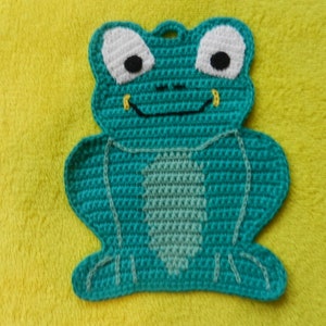 Könnte beinhalten: Ein tealfarbener gehäkelter Frosch-Topflappen mit weißen Augen und einer schwarzen Nase. Der Frosch sitzt auf einer gelben Oberfläche.