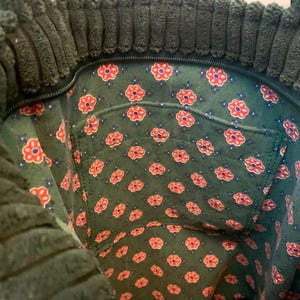 May include: The inside of a green corduroy tote bag with a floral lining. The lining has a small pocket with a zipper.