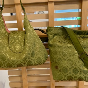 Może przedstawiać: Dwie zielone torebki z tkaniny ze złotymi wzorami kwiatowymi. Jedna to torba na ramię z klapką, a druga to torba na ramię z regulowanym paskiem. Obie torby mają podobny design i schemat kolorów.