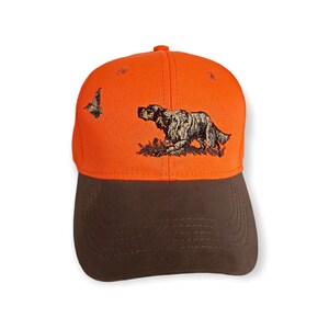 May include: Orange and brown baseball cap with an embroidered image of a dog and a bird.