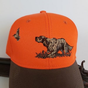 May include: Orange and brown baseball cap with an embroidered image of a dog and a bird.
