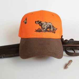 May include: Orange and brown baseball cap with an embroidered image of a hunting dog and a bird. The cap has a brown brim and a bright orange crown.