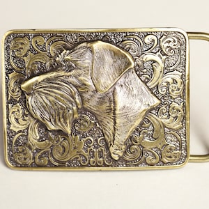 May include: A brass belt buckle with an ornate design featuring a detailed, three-dimensional image of a dog's head.