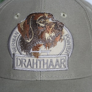 Op de afbeelding: Een groene baseballpet met een geborduurde patch met een Duitse Kortharige Wijzer, de woorden "German Pointer" en "Drahthaar".