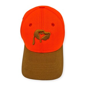 Peut inclure: Une casquette de baseball orange vif avec un motif de chien brodé brun sur le devant. La casquette a une visière brune.