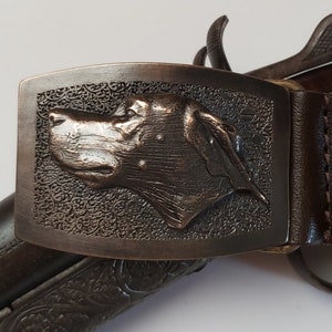May include: A brown leather belt with a metal buckle featuring a detailed embossed dog head design.