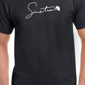 May include: A black t-shirt with a white signature that reads "Sinatra" with a small hat above the "a".
