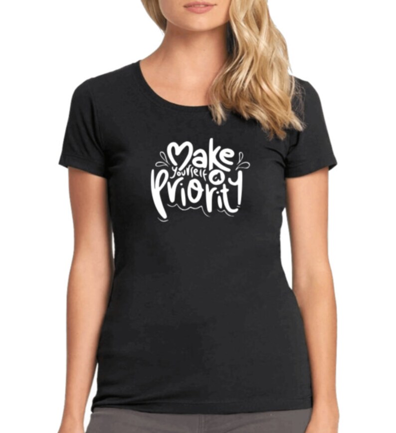 K&ouml;nnte beinhalten: Schwarzes T-Shirt mit wei&szlig;em Text, der in einer stilisierten Schrift "Mach dich selbst zur Priorit&auml;t" lautet.