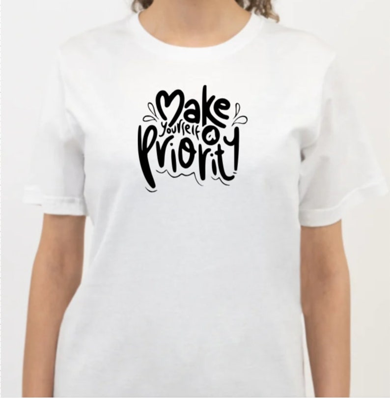 K&ouml;nnte beinhalten: Wei&szlig;es T-Shirt mit schwarzem Text, der "Mach dich zur Priorit&auml;t!" lautet.