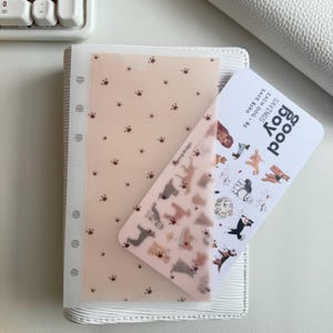 May include: A white binder with a clear pocket containing a light pink sheet with paw prints and a card with dog illustrations and the text "good boy". The card reads "SAVINGS EACH DOG - $5 SAVE $160".