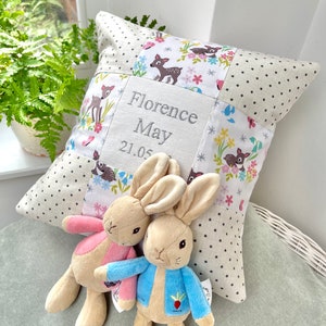 May include: A personalised patchwork cushion embroidered with the name "Florence May" and the date "21.05". The cushion has a deer and floral design. Two plush bunny toys are placed in front of the cushion.