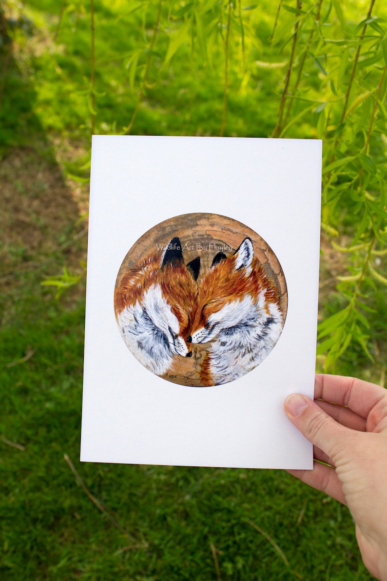 May include: A painting of two foxes cuddling on a wooden background. The foxes are painted in shades of brown, white, and black. The painting is titled "Wildlife Art by Bri Hailey".