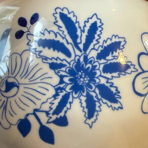 May include: White ceramic vase with a blue floral design. The vase features large, stylized blue flowers and leaves against a white background. The design is detailed and appears to be hand-painted.