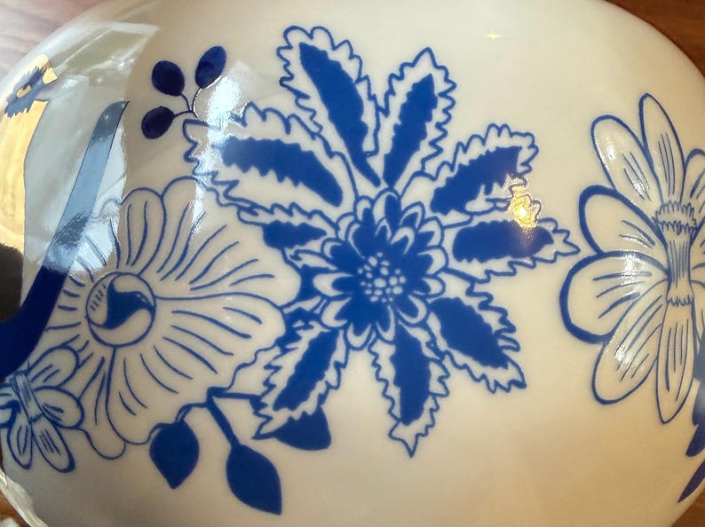 May include: White ceramic vase with a blue floral design. The vase features large, stylized blue flowers and leaves against a white background. The design is detailed and appears to be hand-painted.