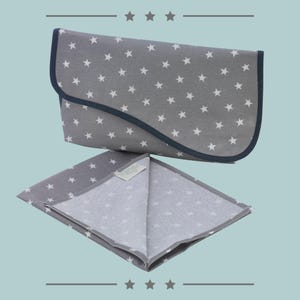May include: A gray changing mat with a white star pattern and a navy blue trim. The mat is folded in half and is lying on a light blue surface.