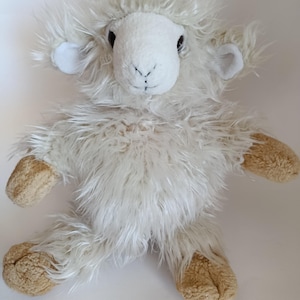May include: A plush, white sheep toy with fluffy fur and tan hooves. The sheep has a white face with black eyes and a stitched mouth. The ears are small and white. The toy is designed to look like a lamb.