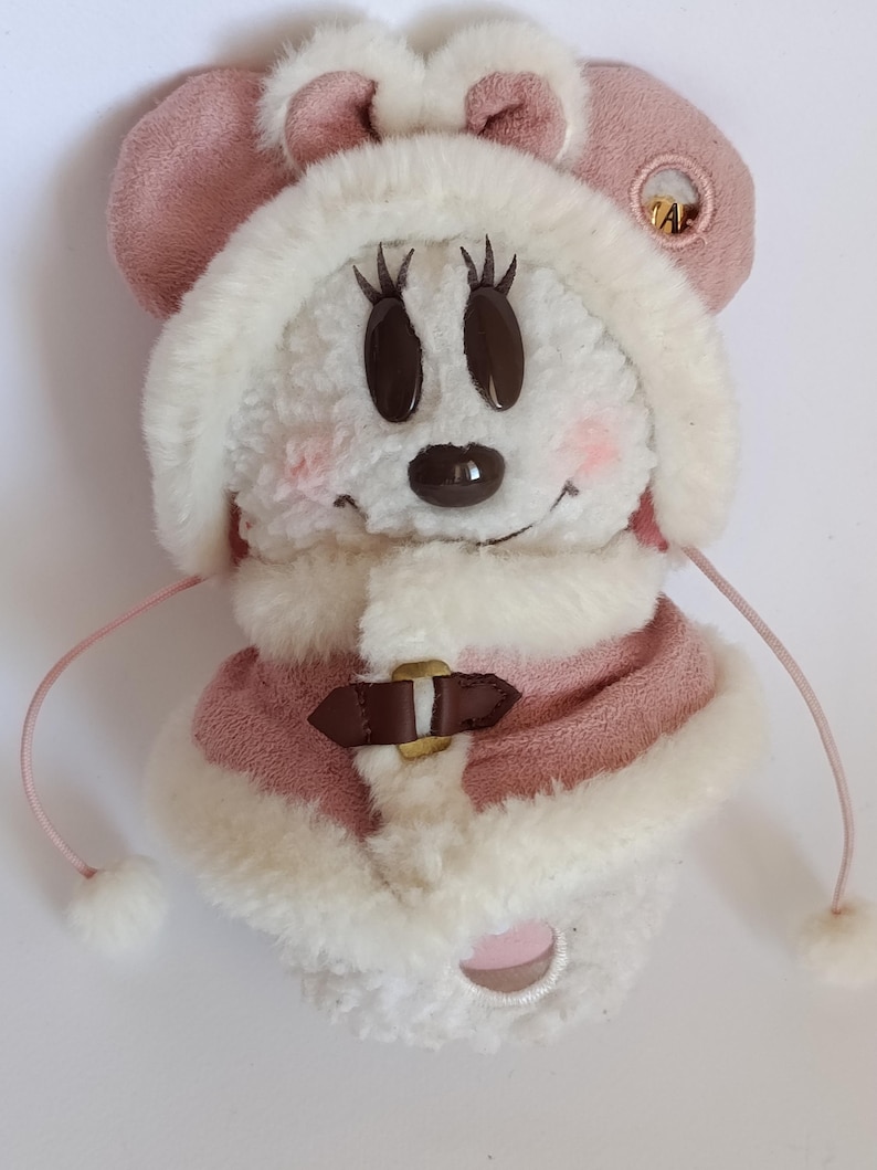 May include: A plush Minnie Mouse character in a winter outfit. The toy features a pink hat with ears, a matching coat with a faux fur trim, and a brown belt. The face has large black eyes and a small black nose.