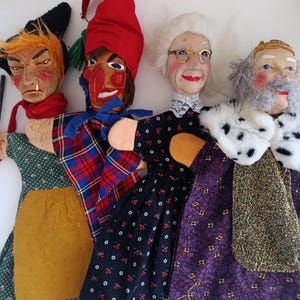 May include: Four hand puppets featuring distinct characters: a figure in a green floral dress with a yellow apron, a figure in a red hat and plaid cape, a figure with white hair and glasses in a black cherry-print dress, and a king in a fur-trimmed robe.