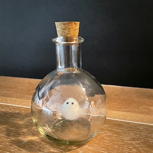 May include: A clear glass bottle with a cork stopper, containing a small white ghost figurine.