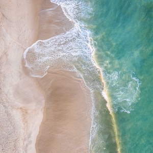 May include: An aerial view of a sandy beach with turquoise water and two people paddleboarding. The water is clear and shallow, and the sand is white and powdery.