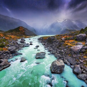May include: A scenic landscape featuring a turquoise river winding through a valley. Large gray rocks line the riverbanks, with mountains in the background under a cloudy sky. The river's water is a vibrant turquoise color.