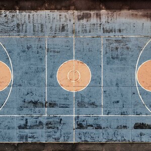 May include: An aerial view of an outdoor basketball court with faded blue paint and white lines. The court has three orange circles in the center, two of which are surrounded by white semi-circles.
