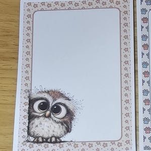 Puede incluir: Una pila de tarjetas de notas en blanco con un borde decorativo y una ilustración de un búho de dibujos animados. El borde es de color marrón claro con pequeños motivos florales. El búho tiene ojos grandes y plumas marrones y blancas.