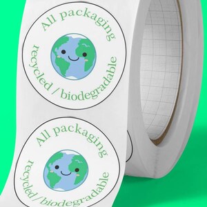 Peut inclure: Un rouleau d'autocollants circulaires blancs avec un dessin de la Terre souriante en vert et bleu. Le texte "All packaging recycled/biodegradable" est imprim&eacute; autour de la Terre. Le fond est vert vif.