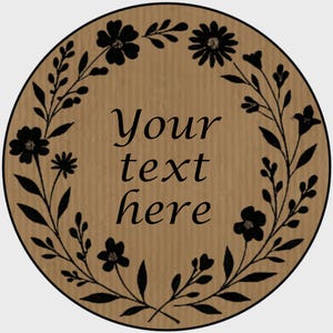 May include: A circular, brown wooden sign featuring a black floral wreath design. The sign has the words "Your text here" in black script in the centre. The floral wreath includes flowers and leaves.