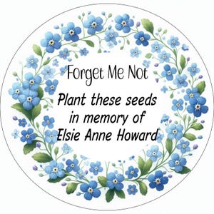 May include: A white circle with a blue forget-me-not flower wreath around the edge. The text "Forget Me Not" is in the centre, followed by "Plant these seeds in memory of Elsie Anne Howard."