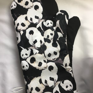 May include: Black and white oven mitt with a panda bear print. The mitt is made of fabric and has a loop for hanging.