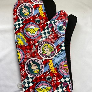 May include: Red and black oven mitt with a checkered pattern and images of Wonder Woman, Superman, and Batgirl. The mitt has the words "BOOM" and "WOOOM" printed on it.