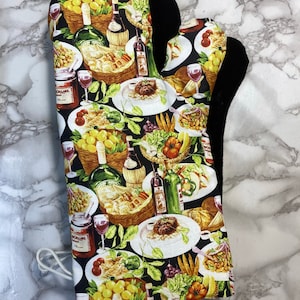 May include: A black oven mitt with a colorful print of food and wine. The print features plates of food, wine bottles, grapes, and other food items. The oven mitt is made of a thick, heat-resistant material.