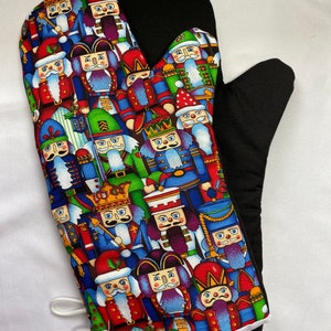 May include: A black and white oven mitt with a colourful pattern of nutcracker figurines. The mitt has a white trim and a loop for hanging.