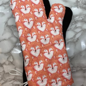 May include: A red and white oven mitt with a fox print. The mitt is lined with black fabric and has a white loop for hanging.