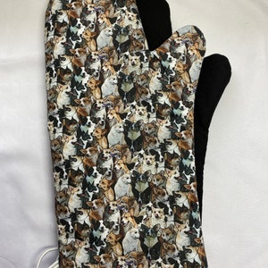 May include: A black and white oven mitt with a pattern of many different dogs. The mitt has a black heat-resistant lining and a white trim around the edge.