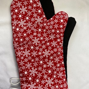 May include: Red oven mitt with a white snowflake pattern. The mitt has a black heat-resistant lining and a white loop for hanging.