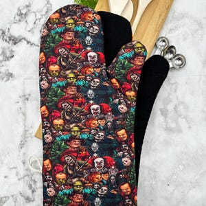 Könnte beinhalten: Ein schwarzer und weißer Ofenhandschuh mit einem bunten Muster aus Horrorfilmfiguren. Der Handschuh ist aus gestepptem Stoff und hat einen weißen Saum.