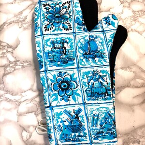 Puede incluir: Manopla de horno azul y blanca con un patrón de azulejos holandeses con molinos de viento, flores y casas. La manopla tiene un forro negro resistente al calor.