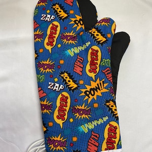 Puede incluir: Una manopla de horno azul con un estampado de cómic con palabras como "¡Super!" y "¡Pow!" en rojo, amarillo y blanco. La manopla tiene un forro negro resistente al calor y un ribete blanco.