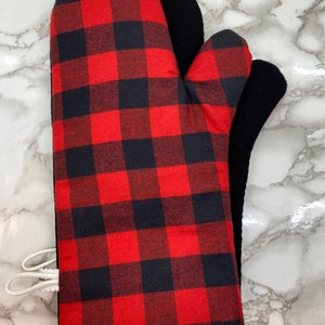 May include: Red and black buffalo check oven mitt with a black heat-resistant lining. The mitt has a white trim around the edge and a white loop for hanging.