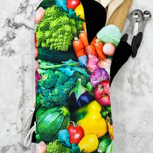 Puede incluir: Un guante de horno colorido con un patrón de varias verduras, incluyendo brócoli, zanahorias, pimientos y tomates.