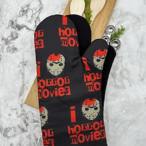 May include: Black oven mitt with a white trim and a repeating pattern of a hockey mask and the text "I love horror movies".