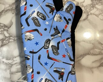 May include: A blue oven mitt with a hockey-themed print. The print features hockey sticks, pucks, skates, and gloves. The mitt has a black heat-resistant lining.